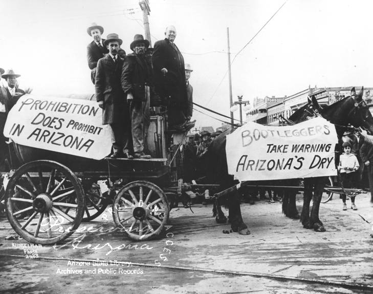 An old, black and white photo of a group of men standing in a wagon that has banners declaring Prohibition was in effect in Arizona.