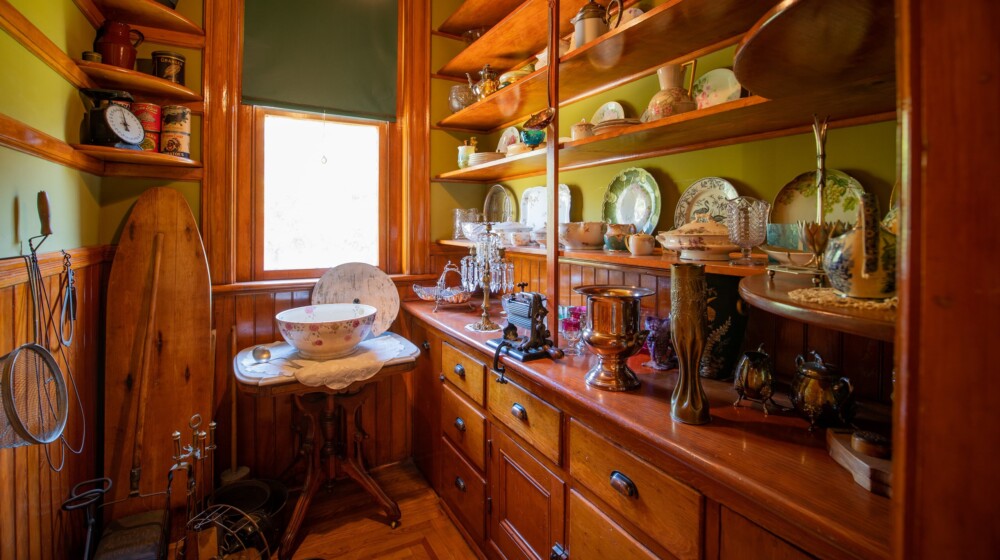 The pantry at Rosson House, with built in cabinets and shelves with many antique pieces of china, glassware, utensils, and other kitchen and cleaning implements.