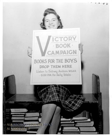 A black and white picture of a woman holding a sign that reads, “Victory Book Campaign, Books for the boys, Drop them here.”