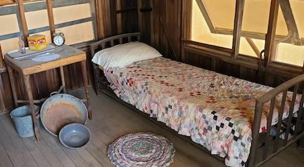 A current day photo of the interior of the tuberculosis cabin at Cave Creek Museum. It has canvas panels over the windows that are shown propped open to allow for better ventilation.